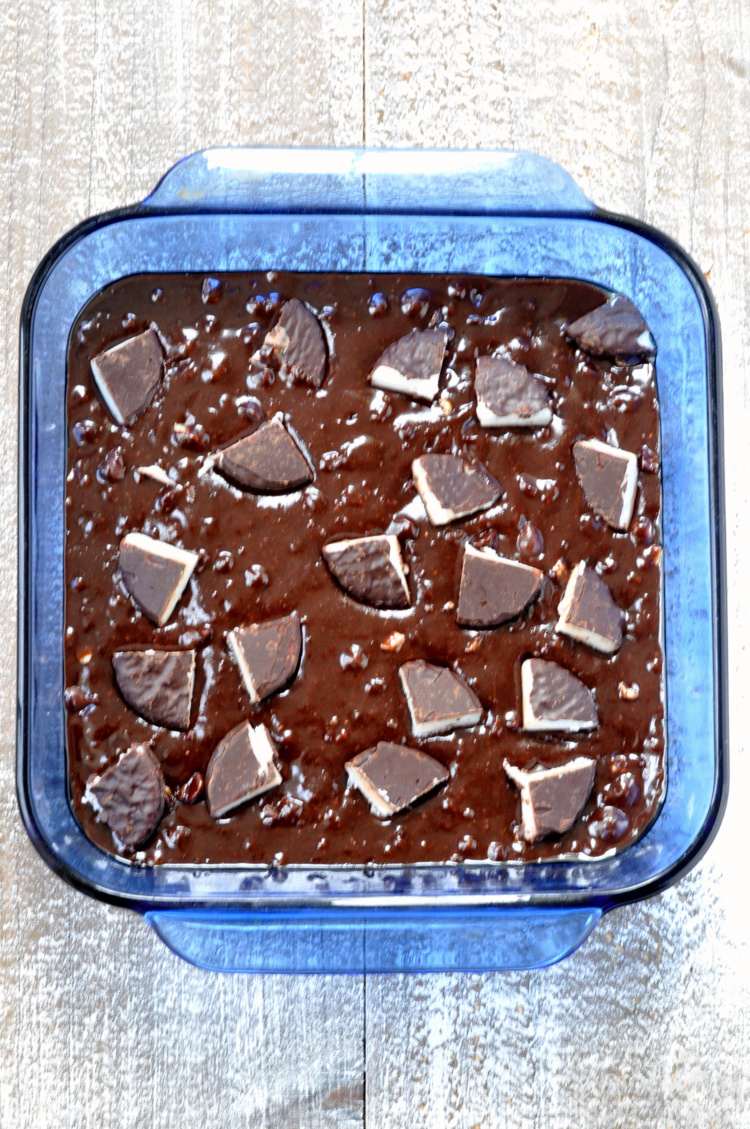 Peppermint patties on top of brownie batter in blue baking dish